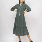 Devojka nosi zelenu haljinu midi dužine sa dugim rukavima i prednjim kopčanjem.