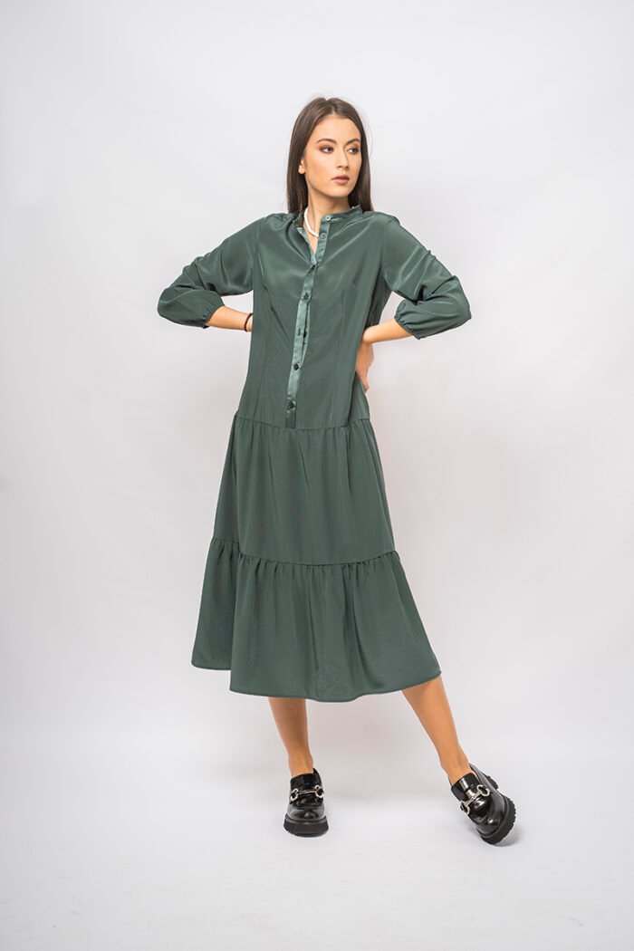 The girl wears a green midi-length dress with long sleeves and a front fastening.