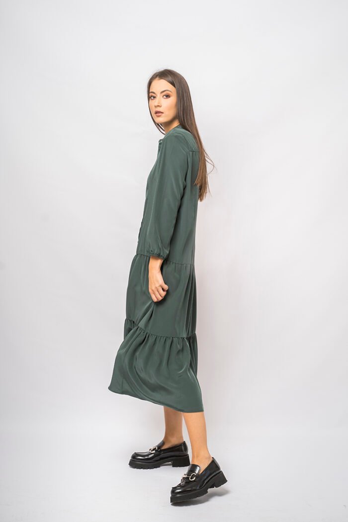 The girl wears a green midi-length dress with long sleeves and a front fastening.