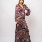 Devojka nosi dugu ljubičastu, dezeniranu haljinu sa dugim rukavima.