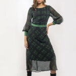 Devojka nosi midi haljinu od zeleno-crnog tartana sa dugim rukavima.