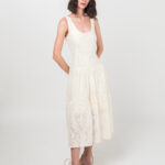 Devojka kratke braon kose nosi elegantnu letnju JOVANA haljinu od pamuka sa floralnom teksturom u bež-beloj boji.