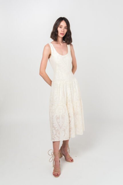 The girl with short brown hair wears an elegant summer JOVANA dress made of cotton with a floral texture in beige and white color.