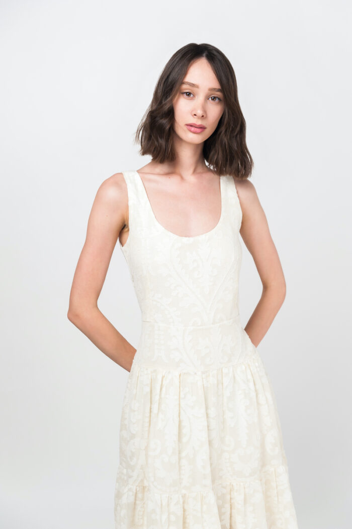 The girl with short brown hair wears an elegant summer JOVANA dress made of cotton with a floral texture in beige and white color.