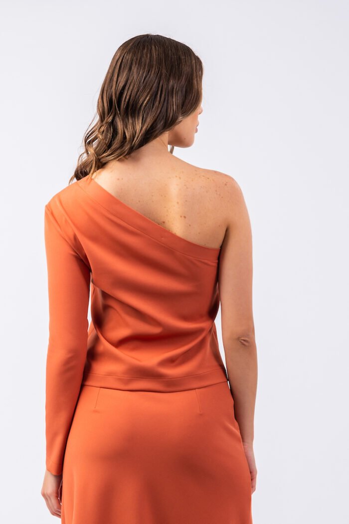 The girl wears an orange INKA top with an asymmetric cut on one shoulder.