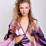 Devojka nosi šarenu, dezeniranu, cvetnu haljinu sa prorezima i kimono rukavima.