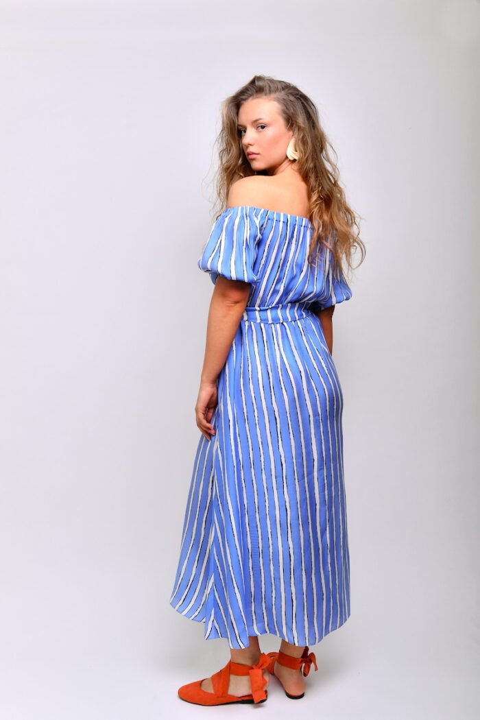 The blonde girl wears a midi blue striped dress made of blue and white silk material.