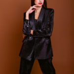 Devojka nosi crni LETITIA blejzer sa sjajnim šljokicama. Stoji ispred tamno crvene pozadine.