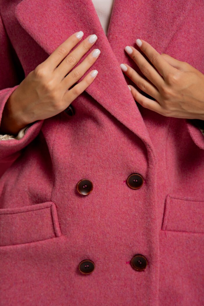 The girl is wearing a pink wool coat with double-breasted closure and standing in front of a pink background