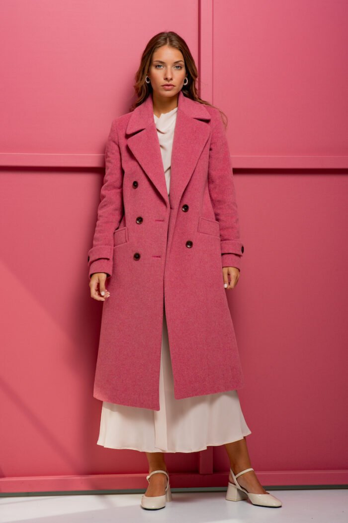 The girl is wearing a pink wool coat with double-breasted closure and standing in front of a pink background