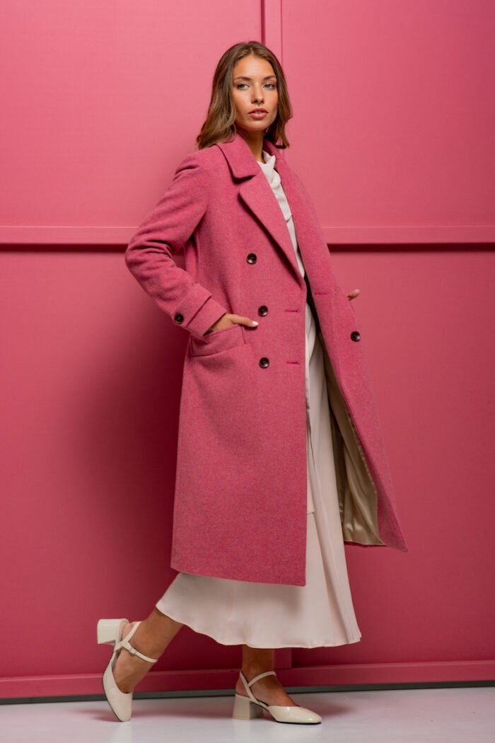 The girl is wearing a pink wool coat with double-breasted closure and standing in front of a pink background