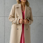 Plava devojka nosi dugački bež kaput sa pink kombinacijom ispod.