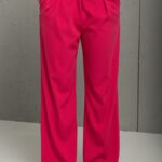 The blonde girl is wearing a pink set with a blazer and SONJA pants, sitting in a white room.