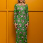 Plava devojka nosi dugu STASHA haljinu od zelene krep viskoze i stoji ispred žute pozadine.