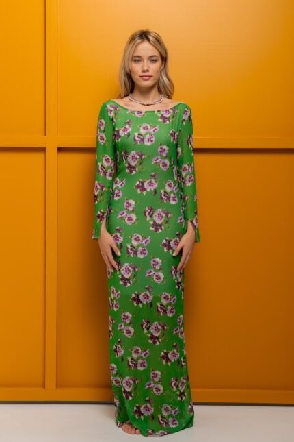 The blonde girl is wearing a long STASHA dress made from green crepe viscose and standing in front of a yellow background.