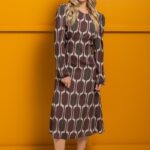 Plava devojka nosi midi TEONA haljinu od svile braon-bež dezena i stoji ispred žutog zida.