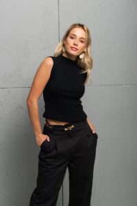 The blonde girl wears a tight black TRIKO sleeveless top with a high neck.