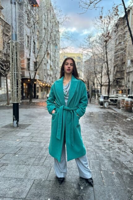 Girl wears tie-waist coat made of soft wool blend in an authentic shade of green.