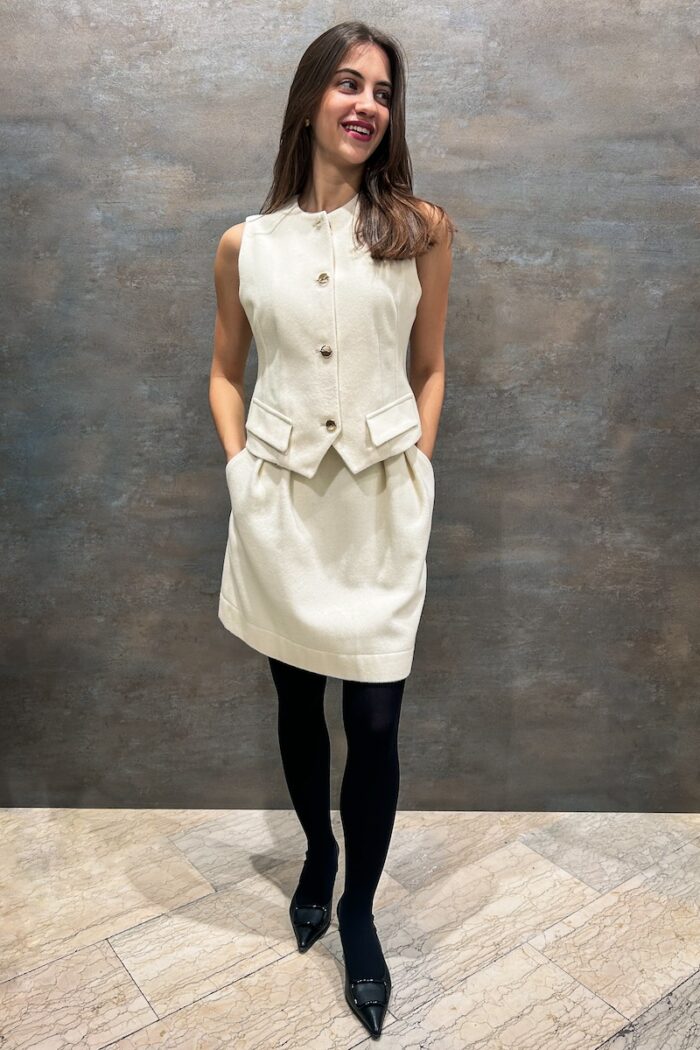 The girl is wearing a white woolen set consisting of a vest and a skirt, paired with black stockings and shoes.