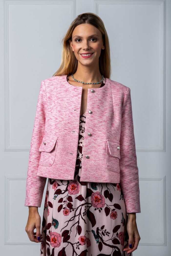 The woman wears a pink cotton blazer and a colorful dress.