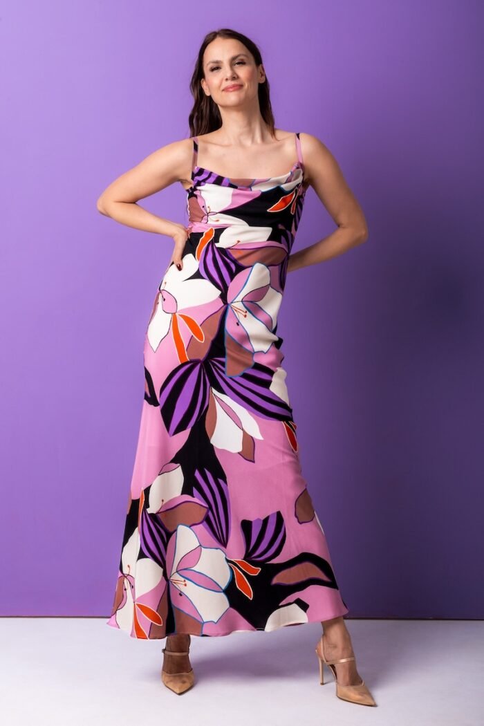 The woman wears a long, silk dress with a floral pattern. He is standing in front of a purple background.