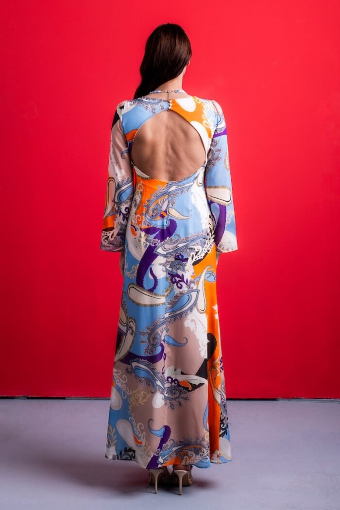 The woman wears a long silk dress with a colorful pattern. She is standing in front of a red background.