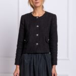 Plava devojka nosi crni blejzer od pamuka i stoji ispred belog zida.