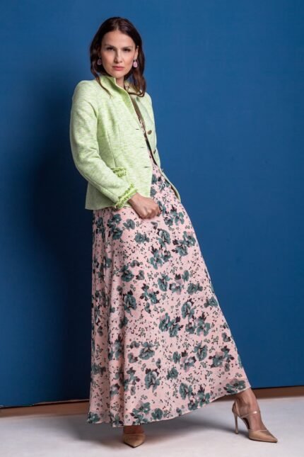 A woman wears a green cotton blazer and floral dress and stands in front of a blue background.