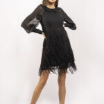 Devojka nosi kratku crnu haljinu sa resama i dugim rukavima.