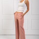 Devojka nosi uske REBECCA pantalone u boji breskve i belu majicu na bretele.