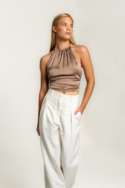 The girl is wearing a beige satin sleeveless top and white pants.