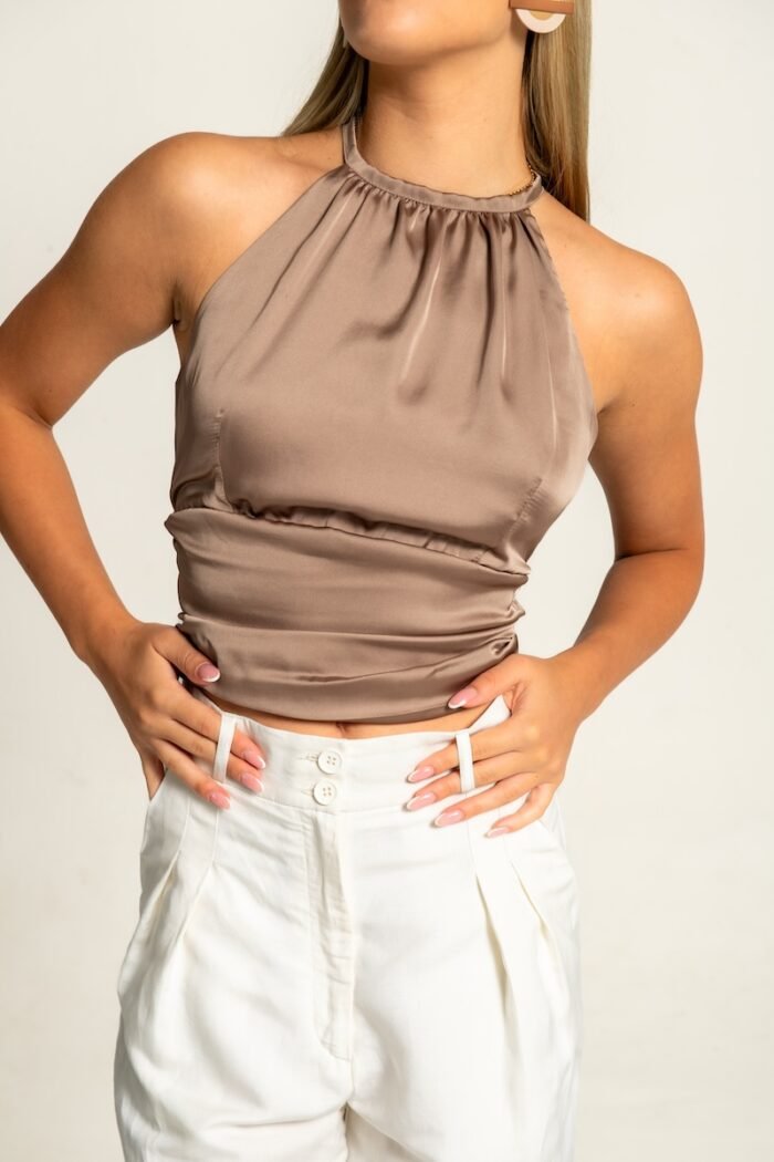 The girl is wearing a beige satin sleeveless top and white pants.