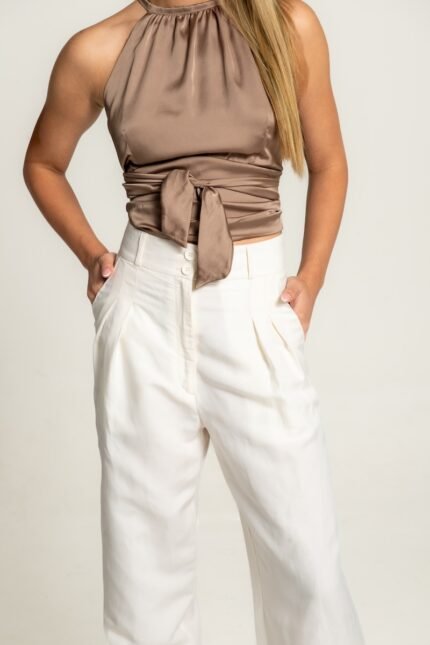 The girl wears white wide leg pants and a satin brown sleeveless top.