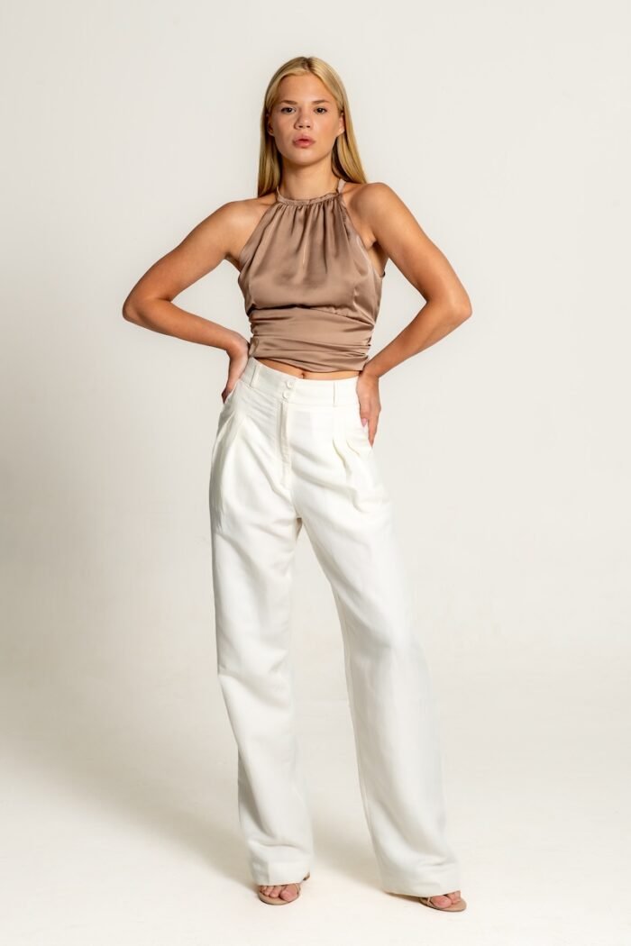 The girl wears white wide leg pants and a satin brown sleeveless top.