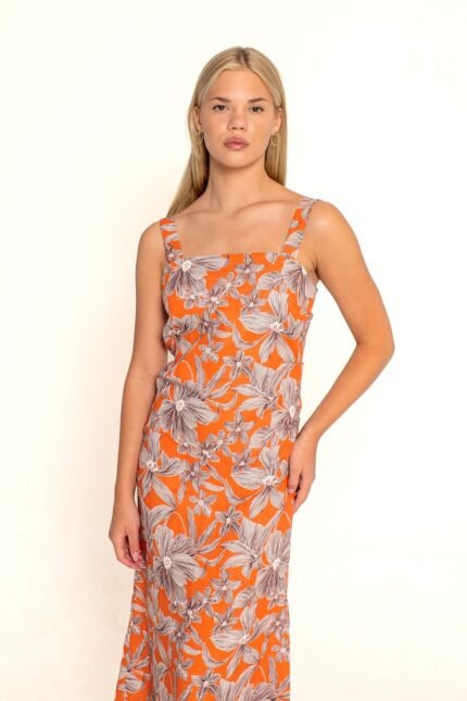 The girl wears a long, orange floral dress with wide straps.