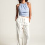 Bele široke lanene pantalone sa elastičnim pojasom i učkurom za vezivanje, kombinovane sa svetloplavim topom na sitne tačkice i bež ravnim cipelama.