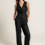 Crne široke lanene pantalone sa elastičnim pojasom i učkurom za vezivanje, stilizovane uz crni laneni prsluk i crne sandale.