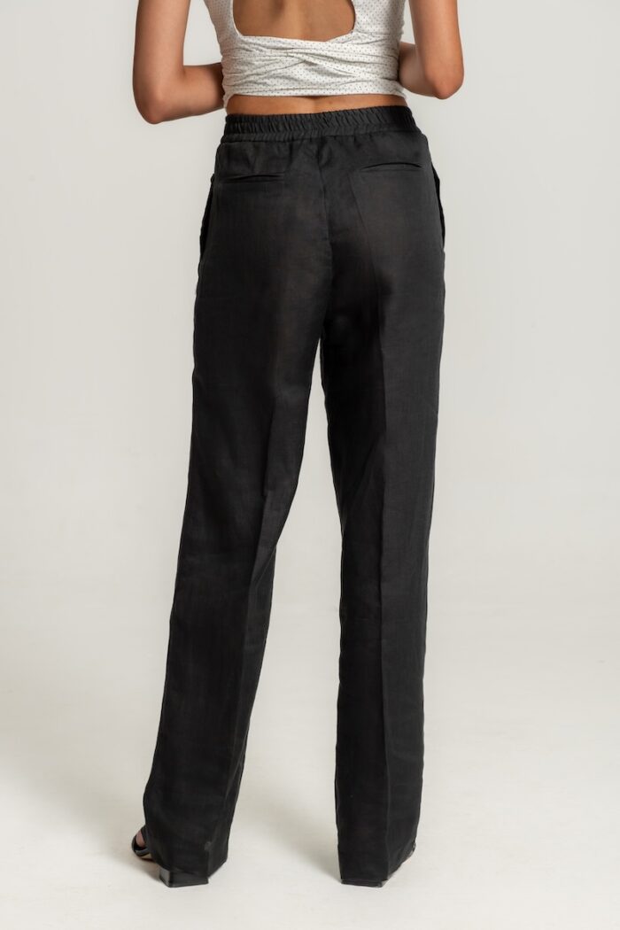 Crne široke lanene pantalone sa elastičnim pojasom i učkurom za vezivanje, stilizovane uz svetli top sa sitnim tačkicama i crne sandale.