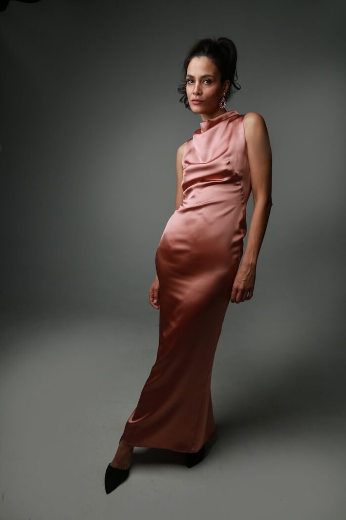 The woman wears a long, brown satin dress