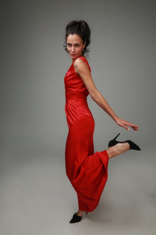 The woman wears a long red V-neck sleeveless dress.