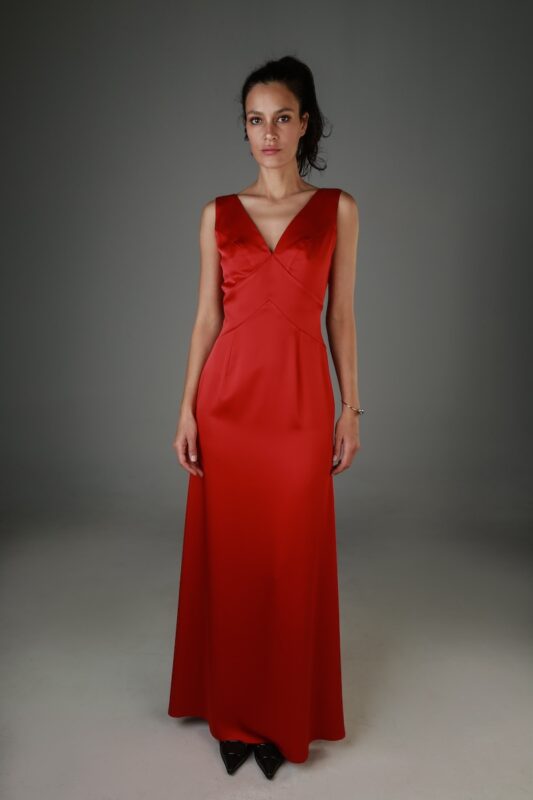 Žena nosi dugu crvenu haljinu bez rukava sa V izrezom.