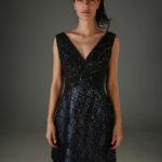 Žena nosi kratku teget-crnu haljinu sa šljokicama i V izrezom.