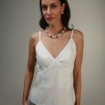 Žena nosi beli top na bretele sa V izrezom.