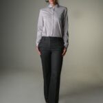 Žena nosi uske tamno sive pantalone i sivu košulju.