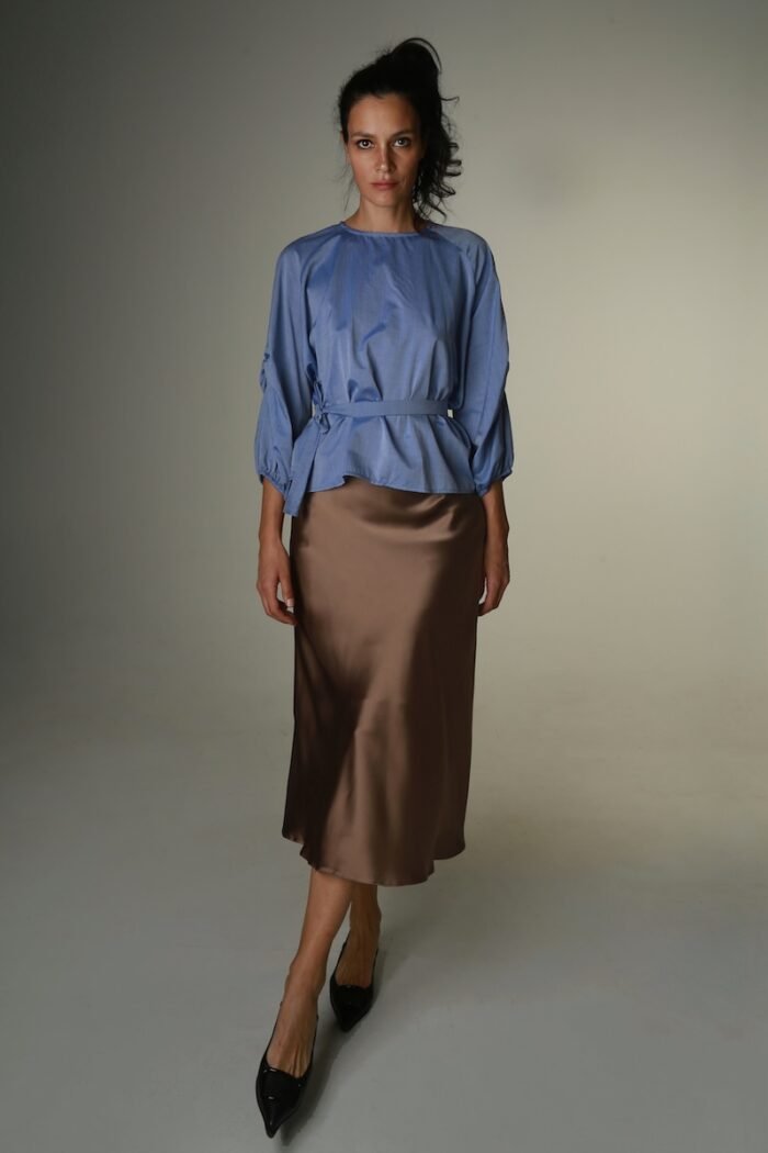 The woman wears a blue blouse with long sleeves and a belt.