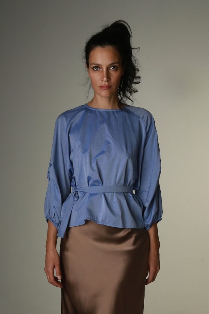 The woman wears a blue blouse with long sleeves and a belt.