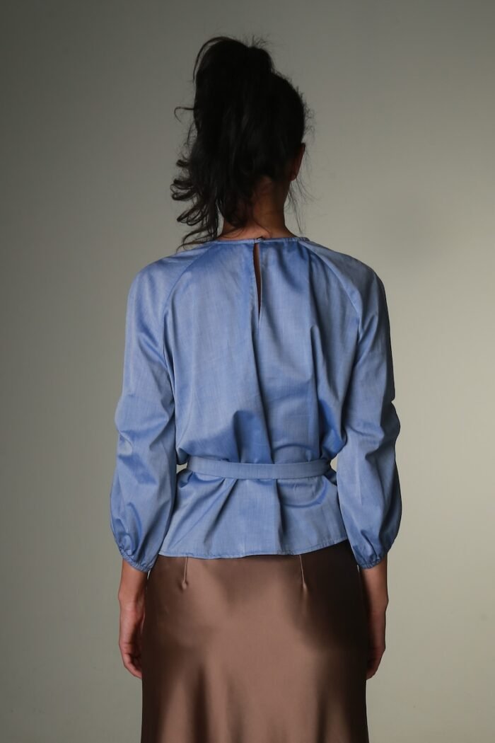 The woman wears a blue blouse with long sleeves and a belt.