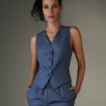 Žena nosi plavi strukirani prsluk i plave pantalone.