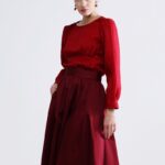 Žena nosi bordo široku suknju i crvenu bluzu sa rukavima.