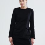 The woman wears a short black dress with long sleeves.